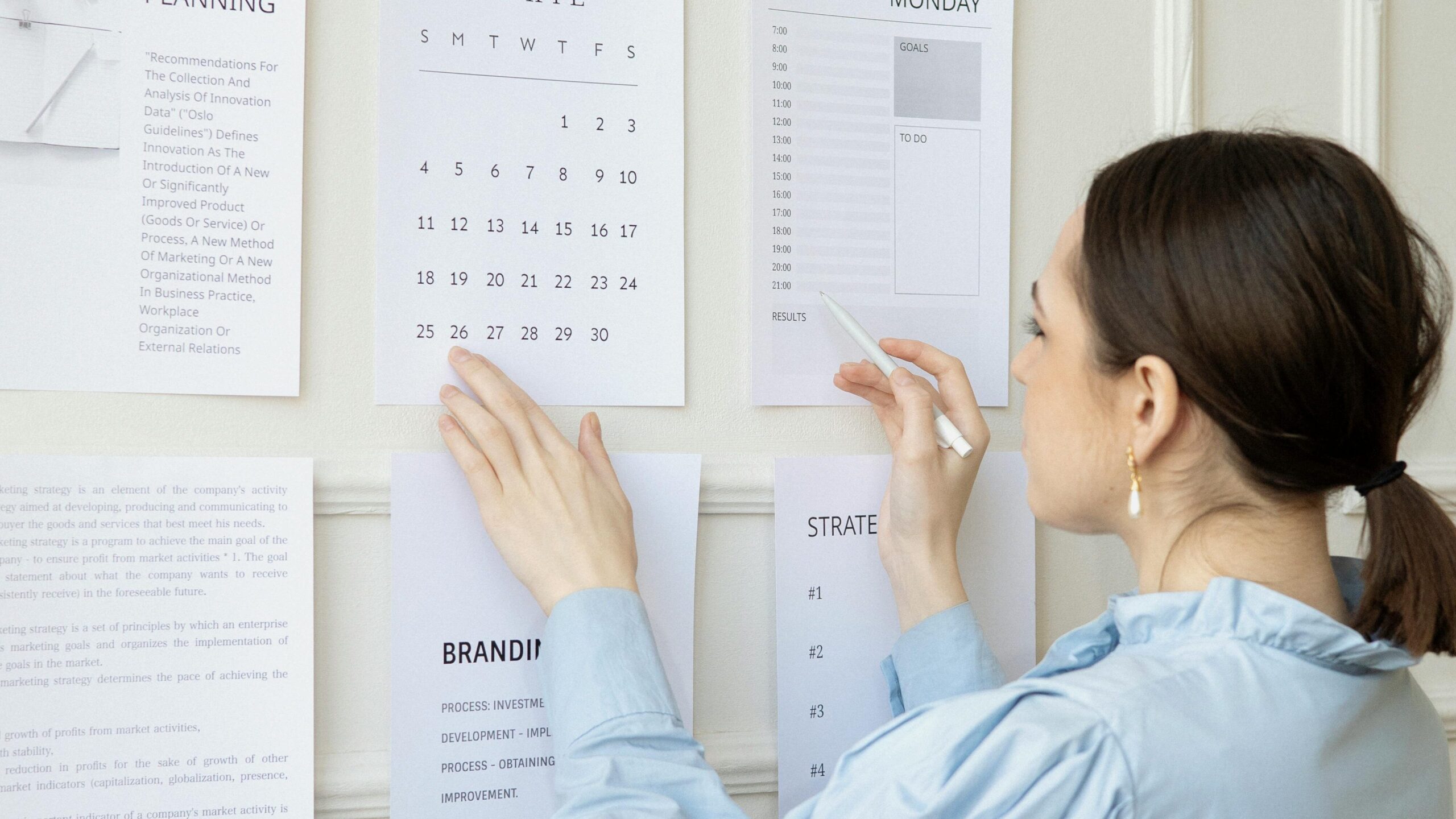 A woman arranging planning documents on an office wall, illustrating business strategy and organization.